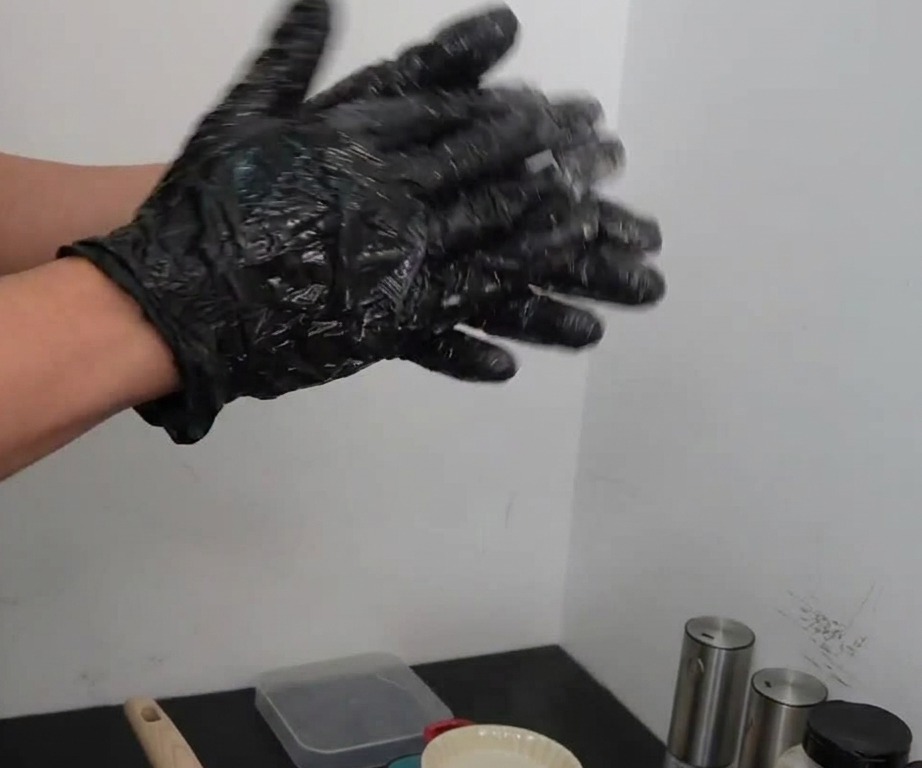 Two gloved hands aggressively tossing and slapping a portioned ball of seasoned raw beef back and forth.