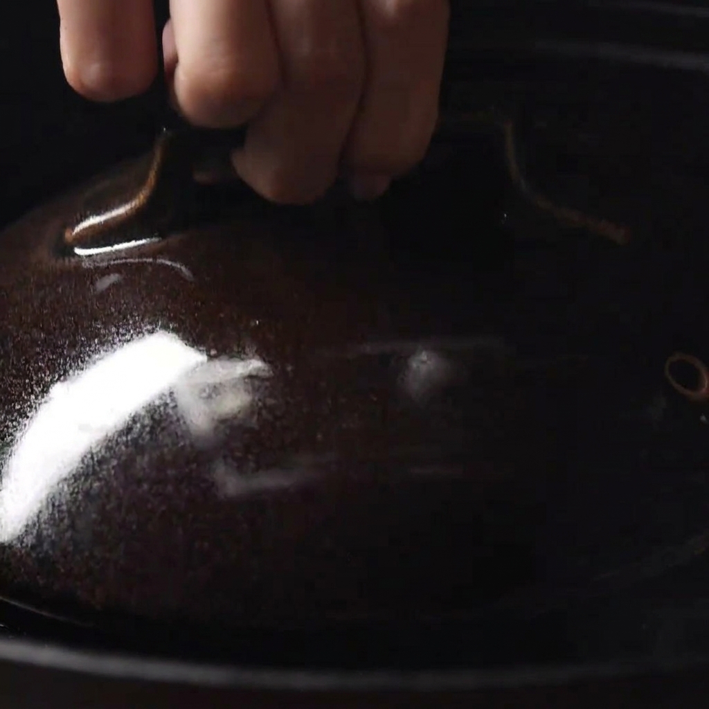 A hand placing a dark ceramic lid over a skillet to trap steam and melt the cheese.