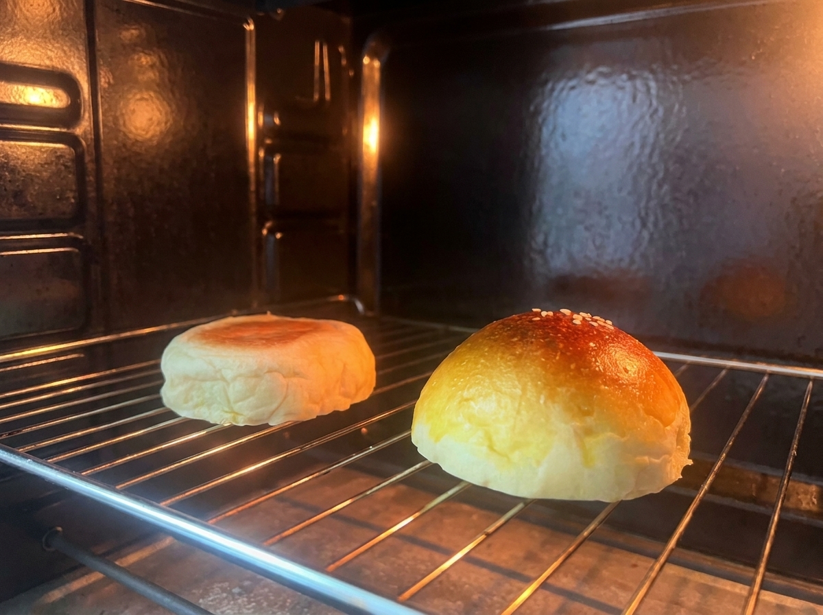 Two halves of a burger bun toasting on a wire rack inside an oven.