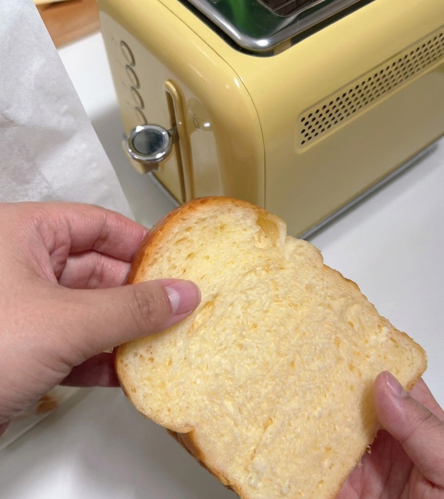 A person inserting a thick slice of white bread into a yellow retro-style toaster.