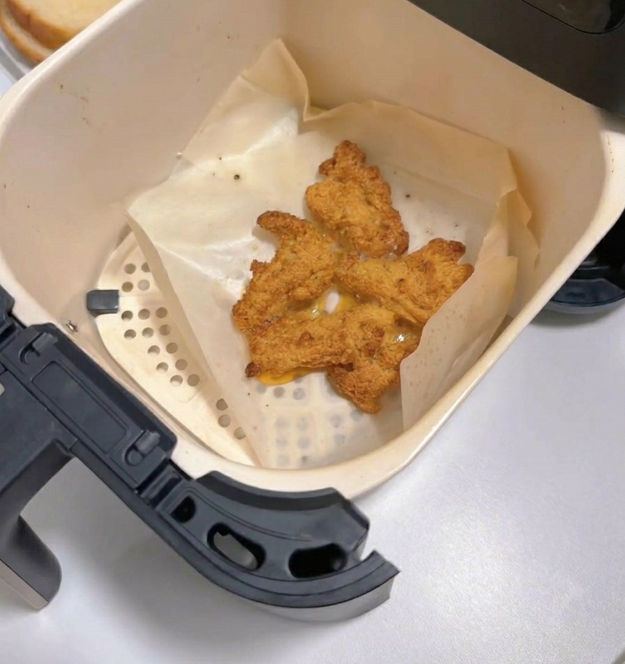 An air fryer drawer pulled out to show several pieces of cooked, crispy golden-brown fried chicken on parchment paper.