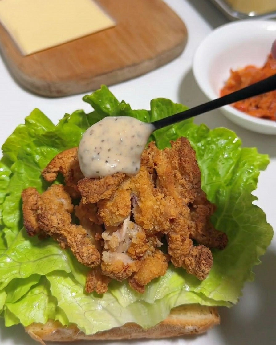 A spoonful of creamy, speckled yuzu pepper mayonnaise being poured over crispy chopped fried chicken on a bed of green lettuce.