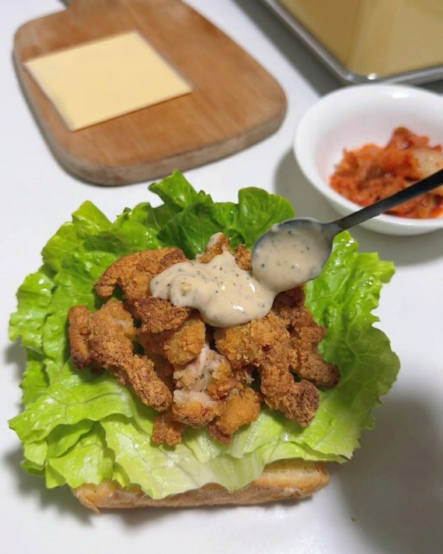 A square slice of yellow cheese resting on top of sauced fried chicken strips and green lettuce.