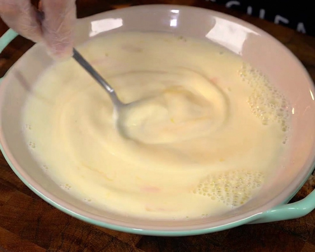 A spoon stirring a yellow egg and milk mixture in a bowl, creating a gentle swirl.