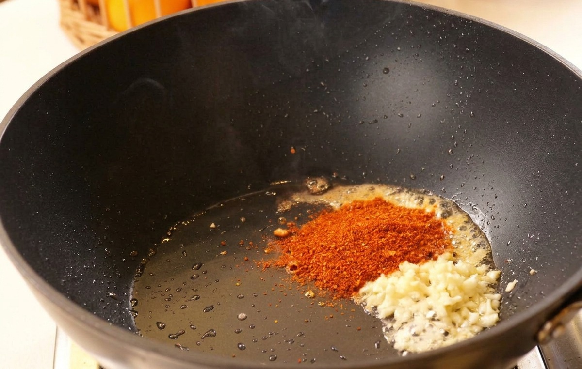 Minced garlic and red chili powder sitting in hot oil in a black wok before being stirred.