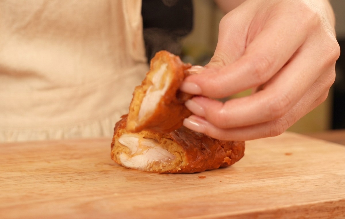 Fingers holding up a halved piece of fried chicken, revealing a thick golden crust and perfectly cooked white meat.