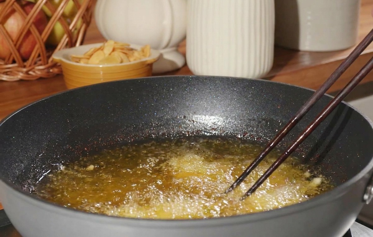 A piece of flour-coated chicken being carefully lowered with chopsticks into a pan of bubbling hot cooking oil.