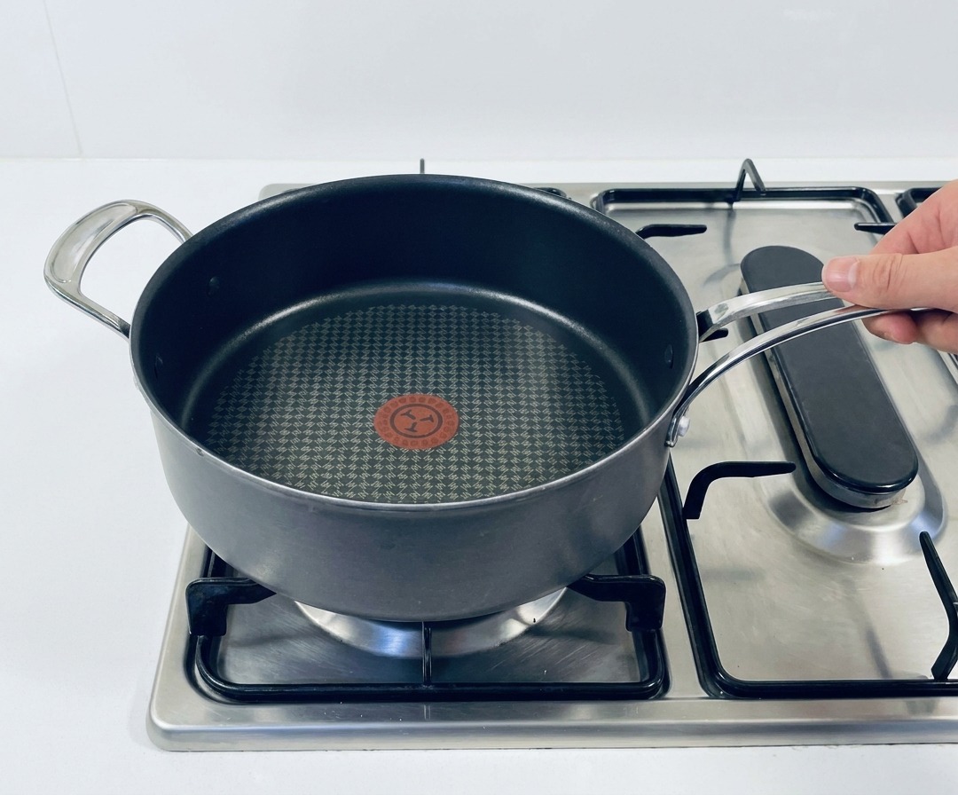 A dark non-stick skillet sitting on a stainless steel gas stove top with the burner turned on.