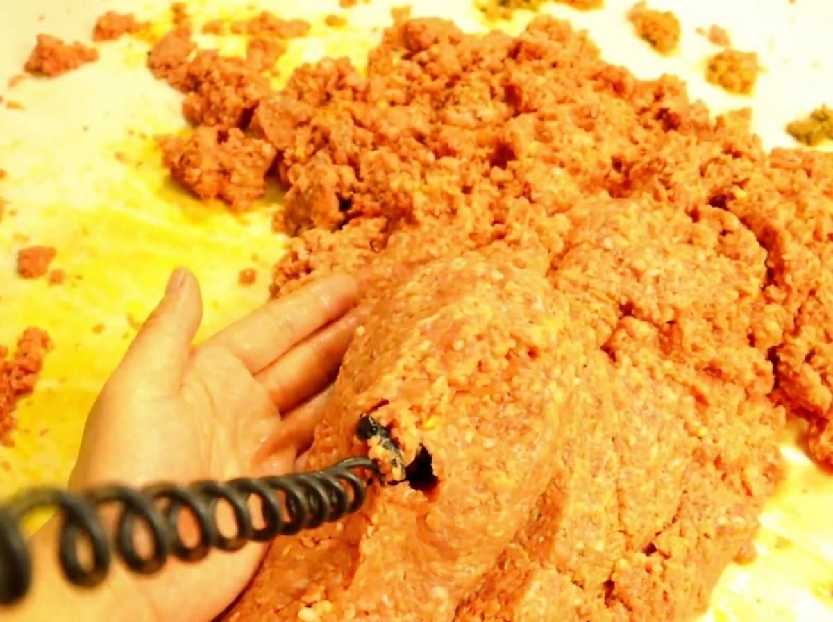 A wooden spoon scooping hot and saucy meat mixture onto a toasted hamburger bun.