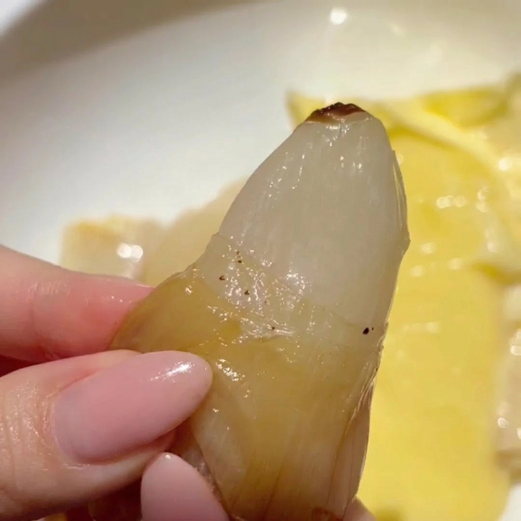 A hand squeezing a single clove of golden, translucent roasted garlic from its papery skin.