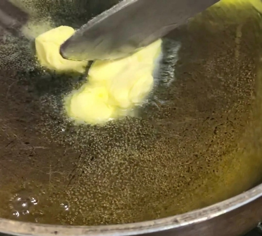 Yellow butter cubes melting and bubbling in a dark, textured skillet over a low flame.