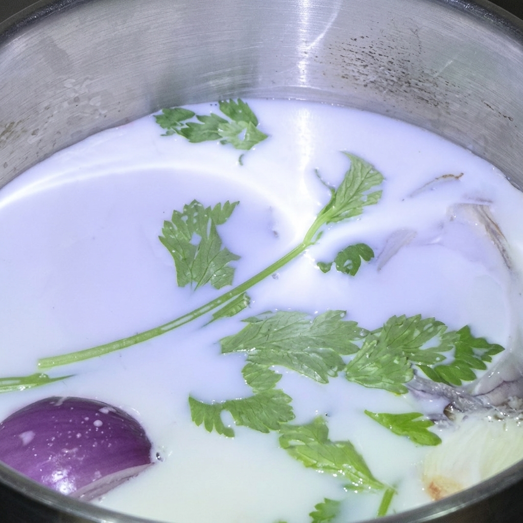 Fresh green herbs and a purple onion wedge floating in a stainless steel pot filled with white milk.