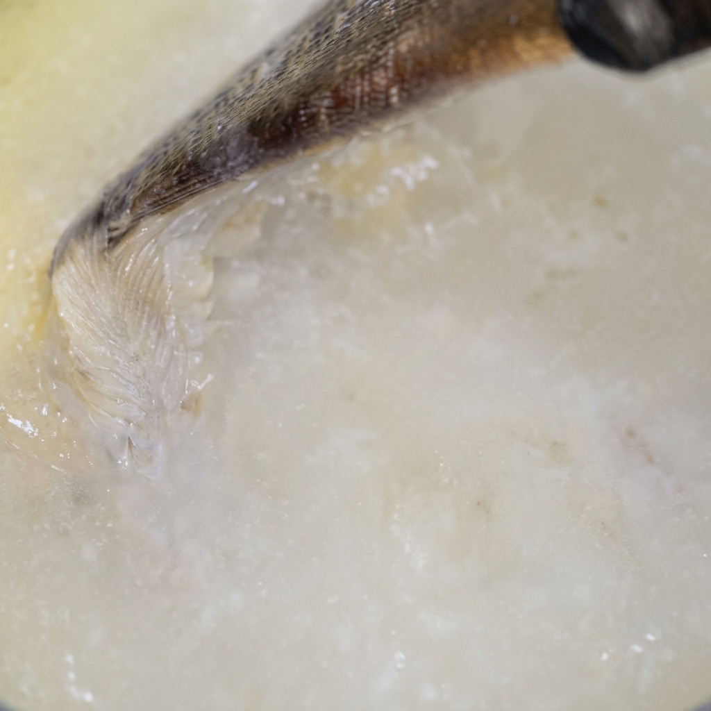 A pale liquid being poured into a pan and mixed with a wooden tool, creating a creamy white base.