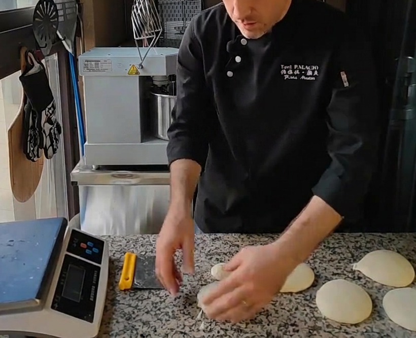 Multiple smooth round balls of pizza dough arranged on a granite countertop after being shaped by hand.