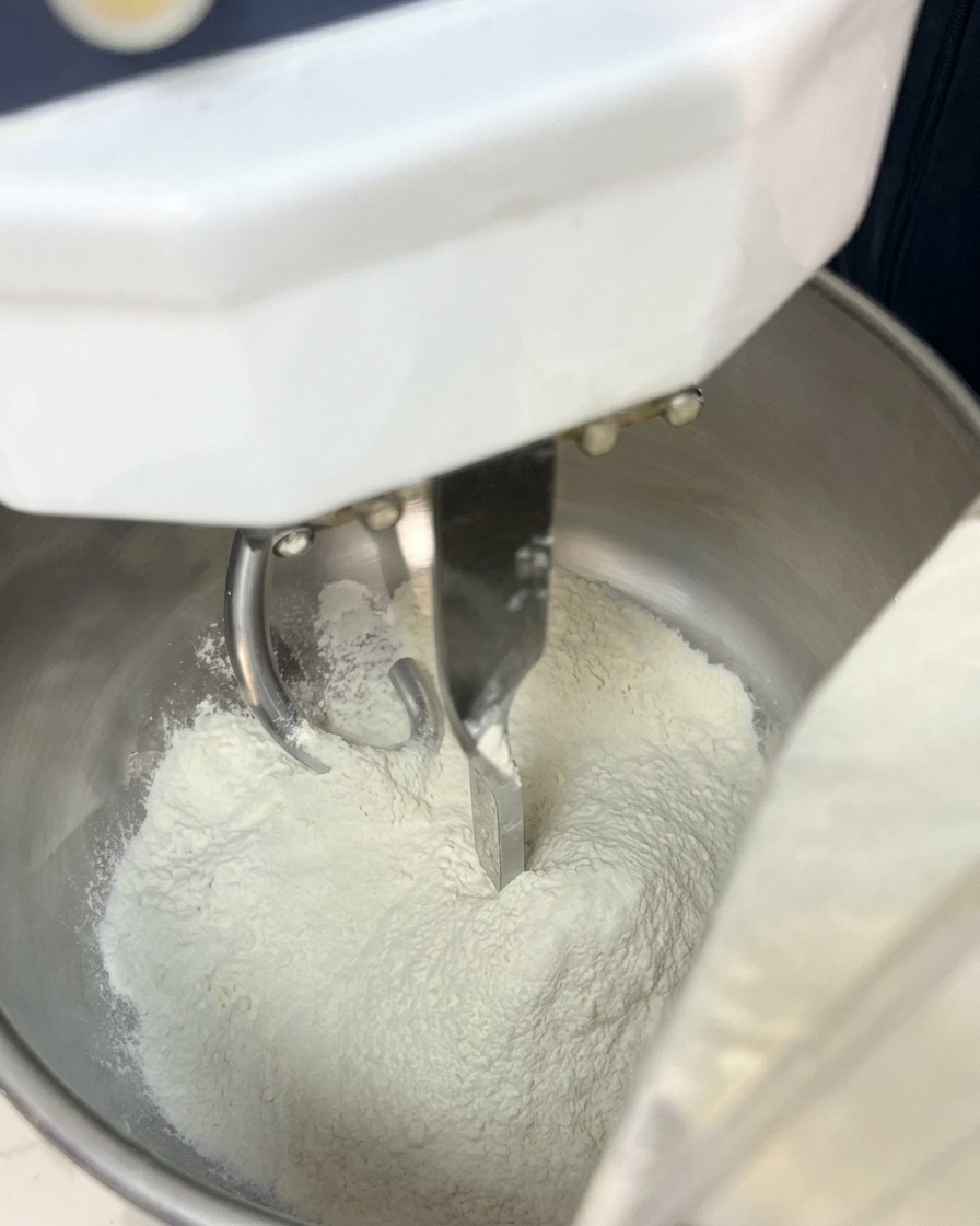 White flour sitting in the metal bowl of a spiral dough mixer.