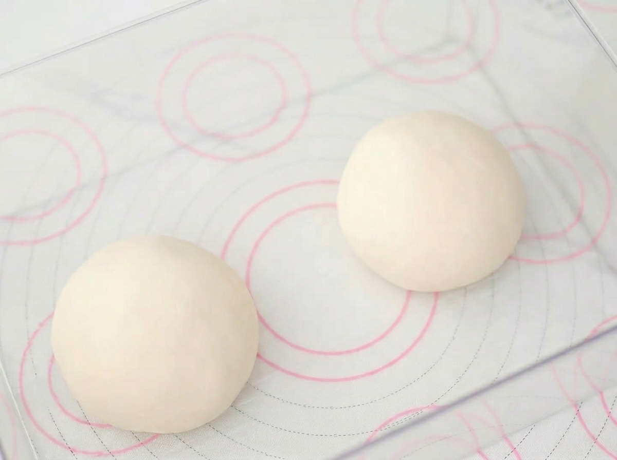 Two smooth round dough balls resting inside a transparent rectangular fermentation container.