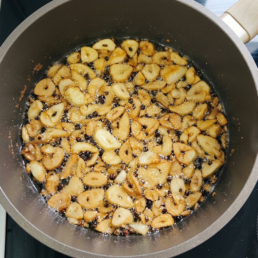 Thin slices of garlic sizzling in a shallow pan of oil, turning a crispy golden brown color.