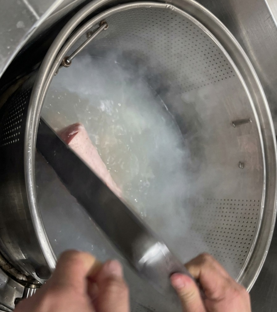 Clean, pale pork trotters being lowered into a metal mesh basket inside a large pot of clear boiling water.