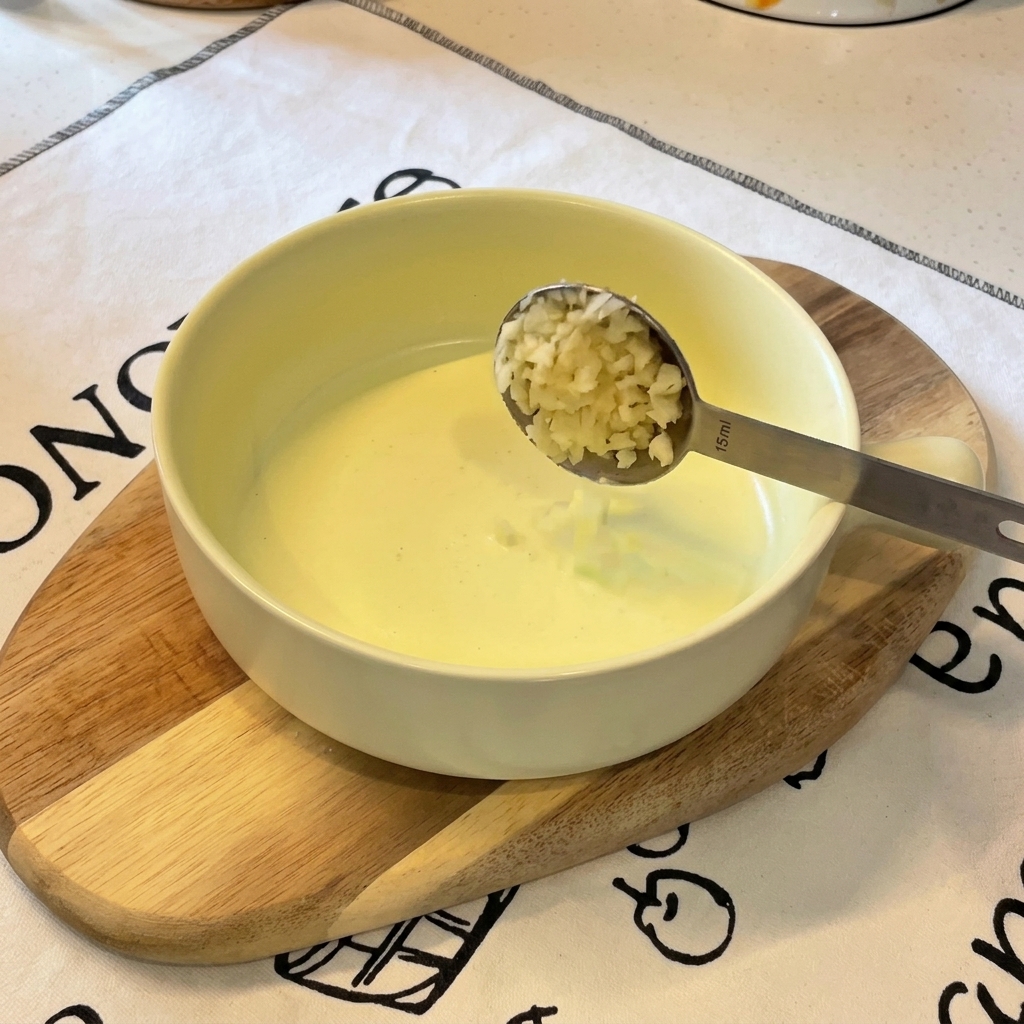 A metal measuring spoon dumping minced garlic into a bowl that already contains a small amount of chopped green onions.