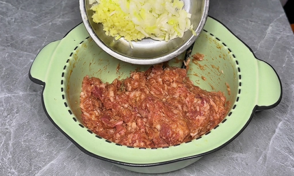 A hand holding a small stainless steel dish of chopped green onions and ginger over a bowl of seasoned meat.