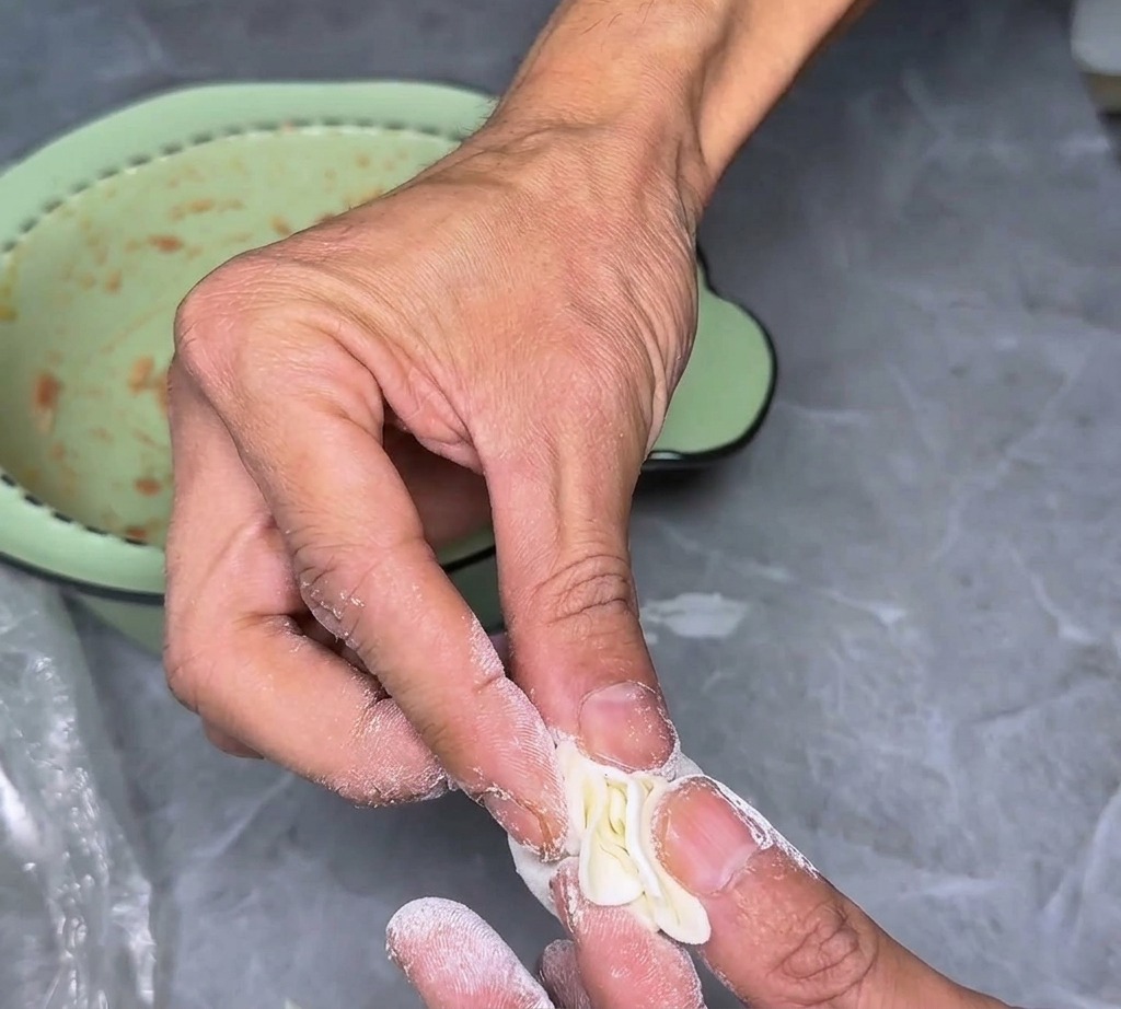 Close-up of fingers pinching the pleated edges of a wonton wrapper to create a decorative and functional seal.