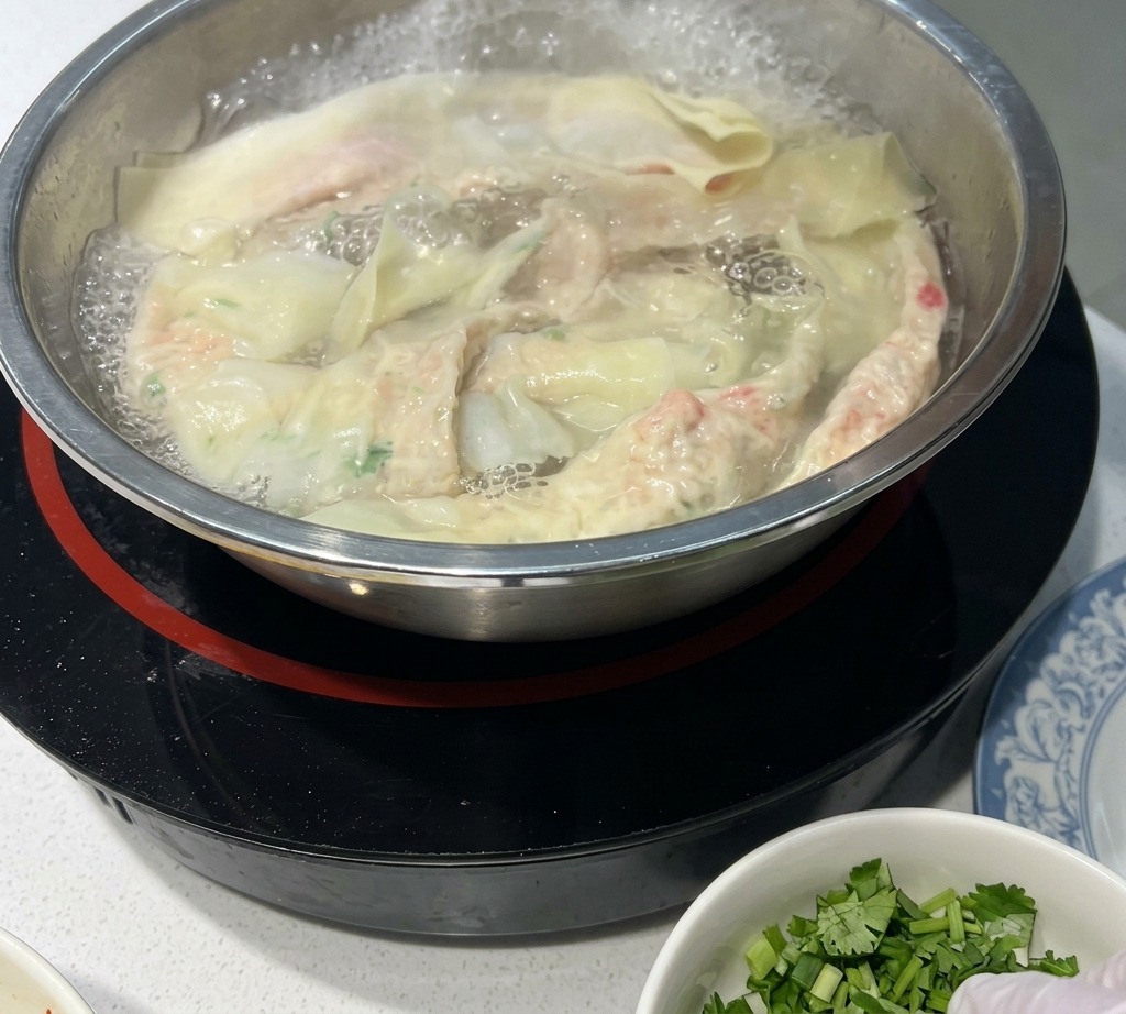 Hand-pulled wonton noodles cooking in a stainless steel pot of bubbling water, with some noodles floating on the surface.