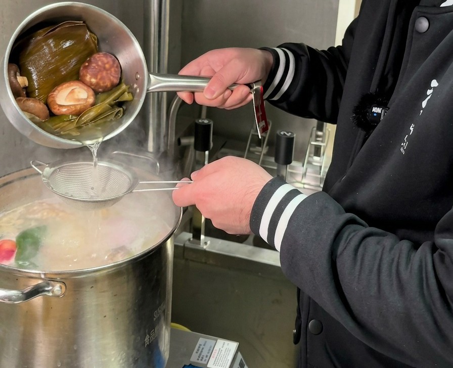Pouring a golden-hued mushroom and kombu infusion through a sieve into a large pot of boiling broth.