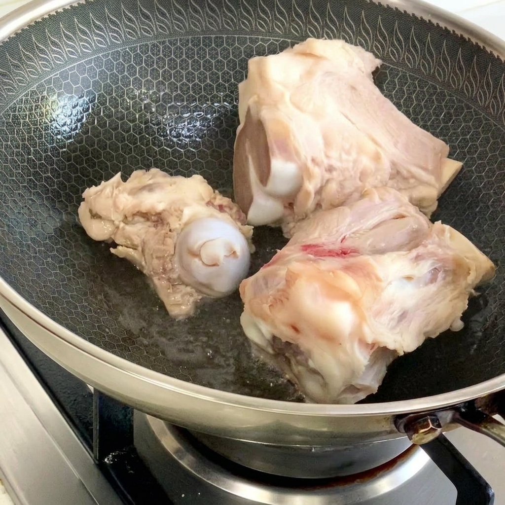 Pork bones being seared in a honeycomb-pattern wok with a small amount of oil.
