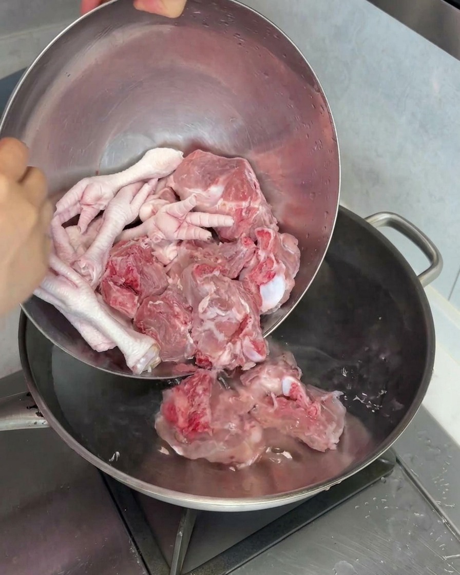 Raw pork marrow bones and chicken feet being placed into a pot of water for blanching.
