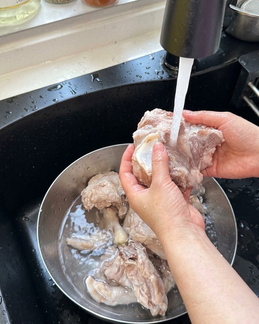 Blanched pork bones and chicken feet being rinsed under warm running water.