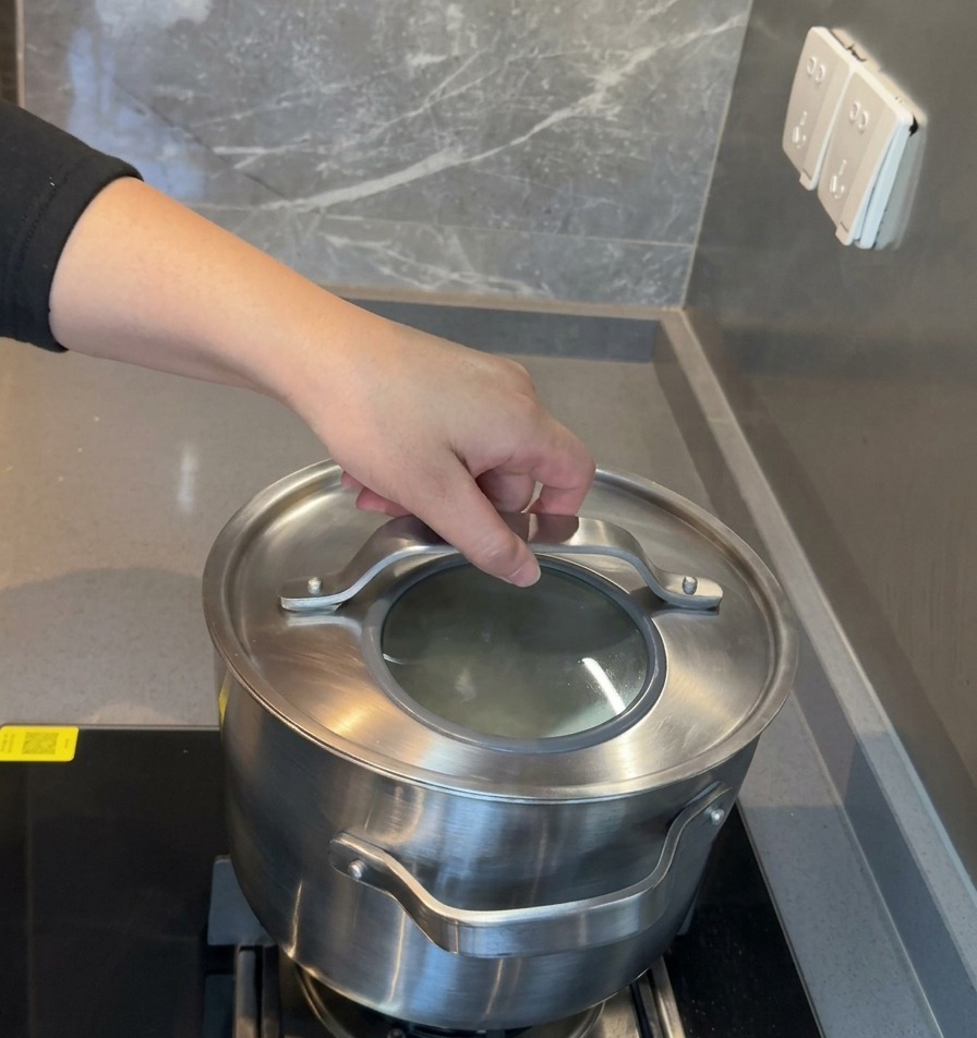 A hand placing a stainless steel rimmed glass lid onto a large pot to begin a long simmering process.