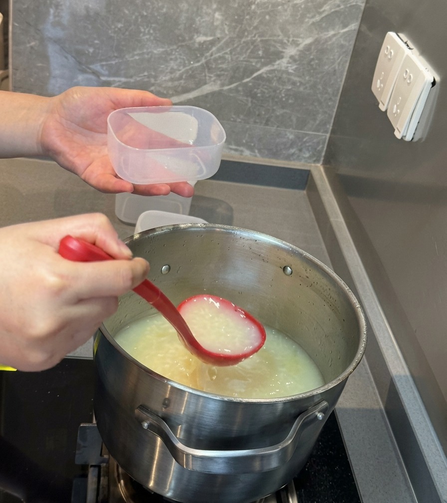 A red ladle pouring rich, white pork bone soup into a small clear plastic storage container.