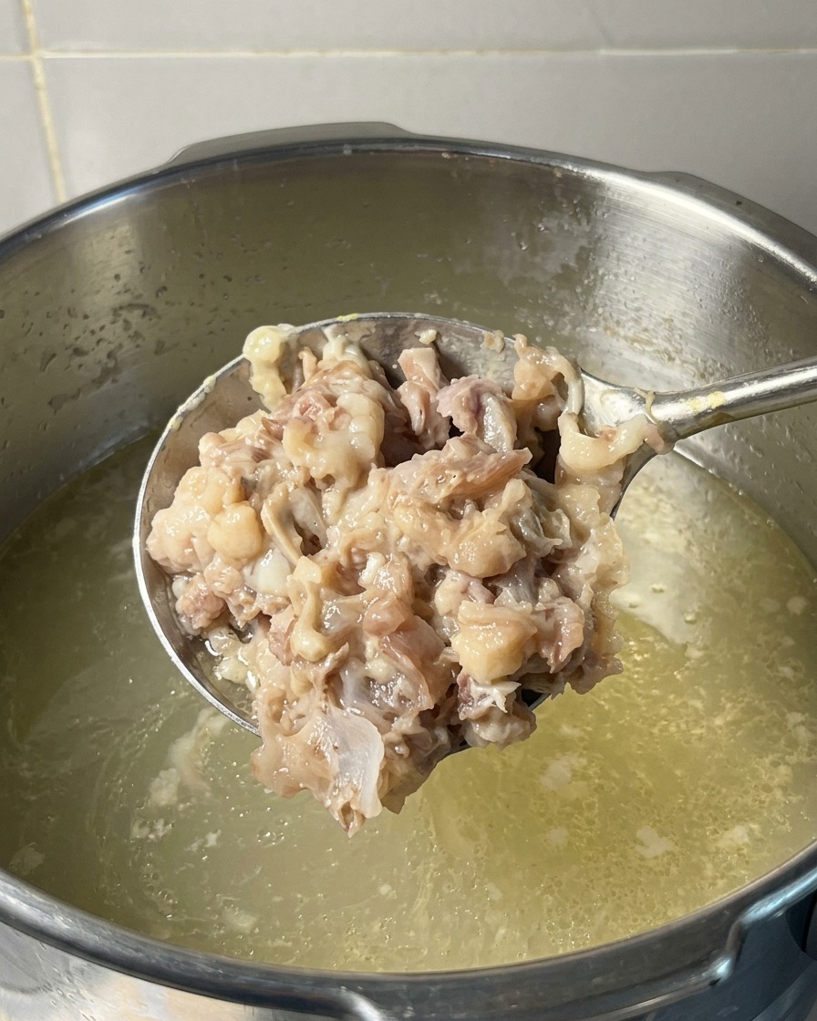 A ladle full of thick, mashed pork and chicken meat being held over a pot of simmering broth.
