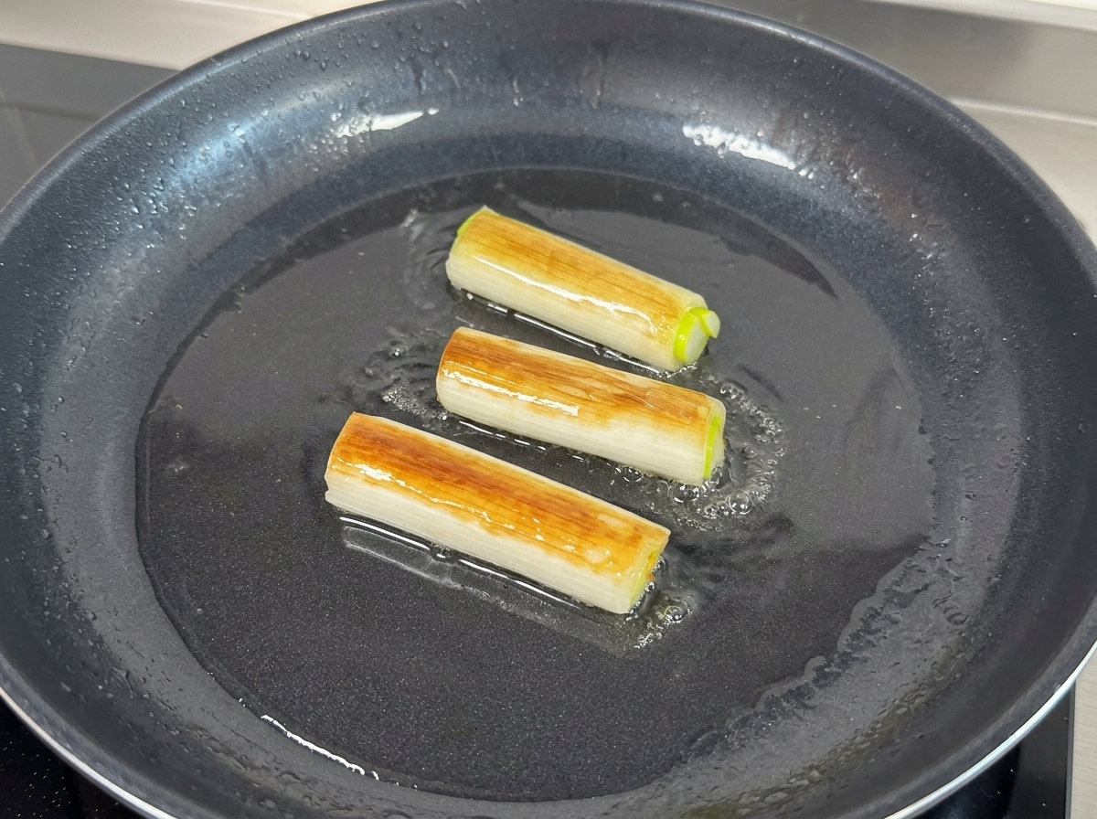 Three large green scallion pieces frying and browning in oil within a black pancite: 60.