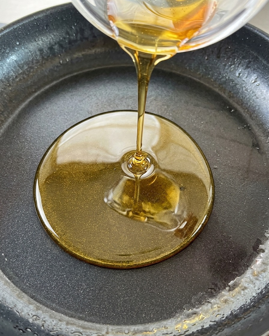 Sesame oil being poured from a small bowl into a pan of hot rendered fatcite: 60.