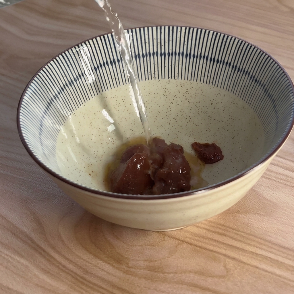 Hot water being poured from above into a blue and white striped bowl containing brown miso paste.