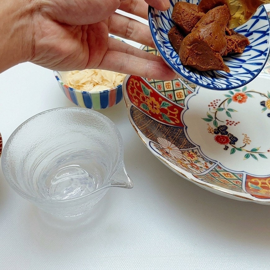 A golden spoon scooping thick, textured brown miso paste into a blue and white patterned porcelain bowl.