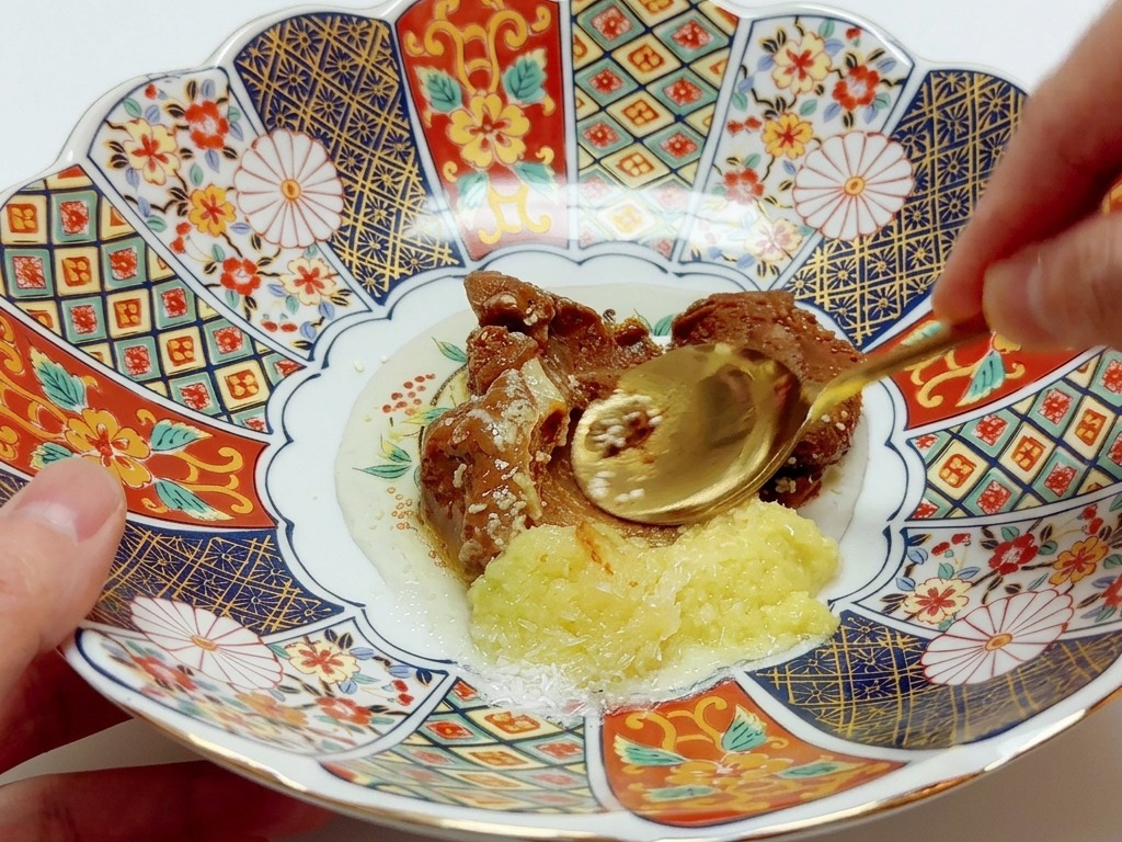 A spoon mixing various pastes and seasonings together in a colorful, ornate porcelain bowl.