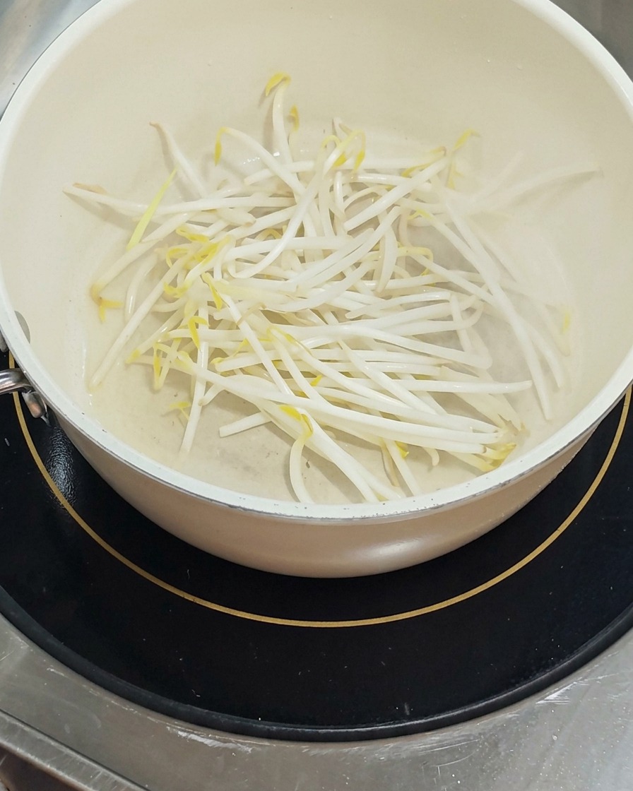 A pile of fresh, white bean sprouts sits in the bottom of a white pot, lightly shimmering with oil.