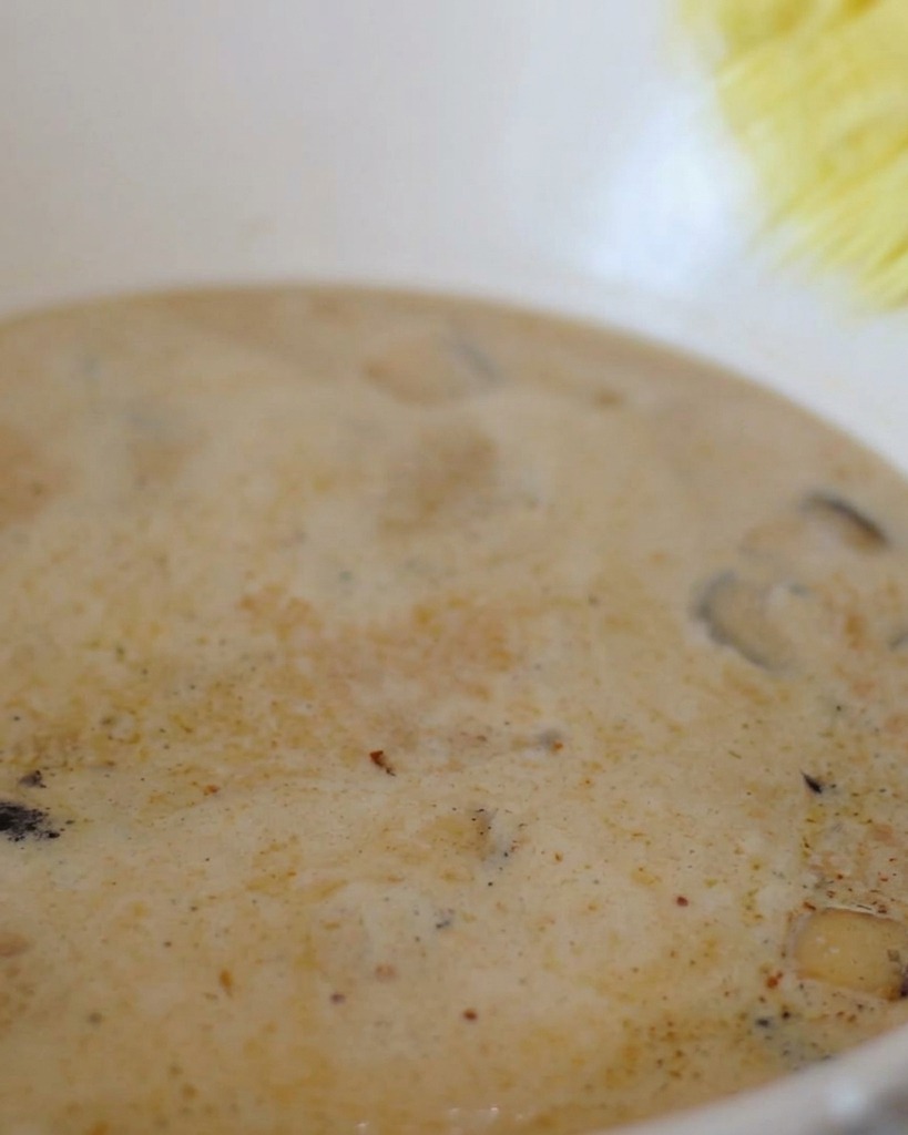 A block of yellow instant ramen noodles being dropped into a pot of bubbling creamy white broth.