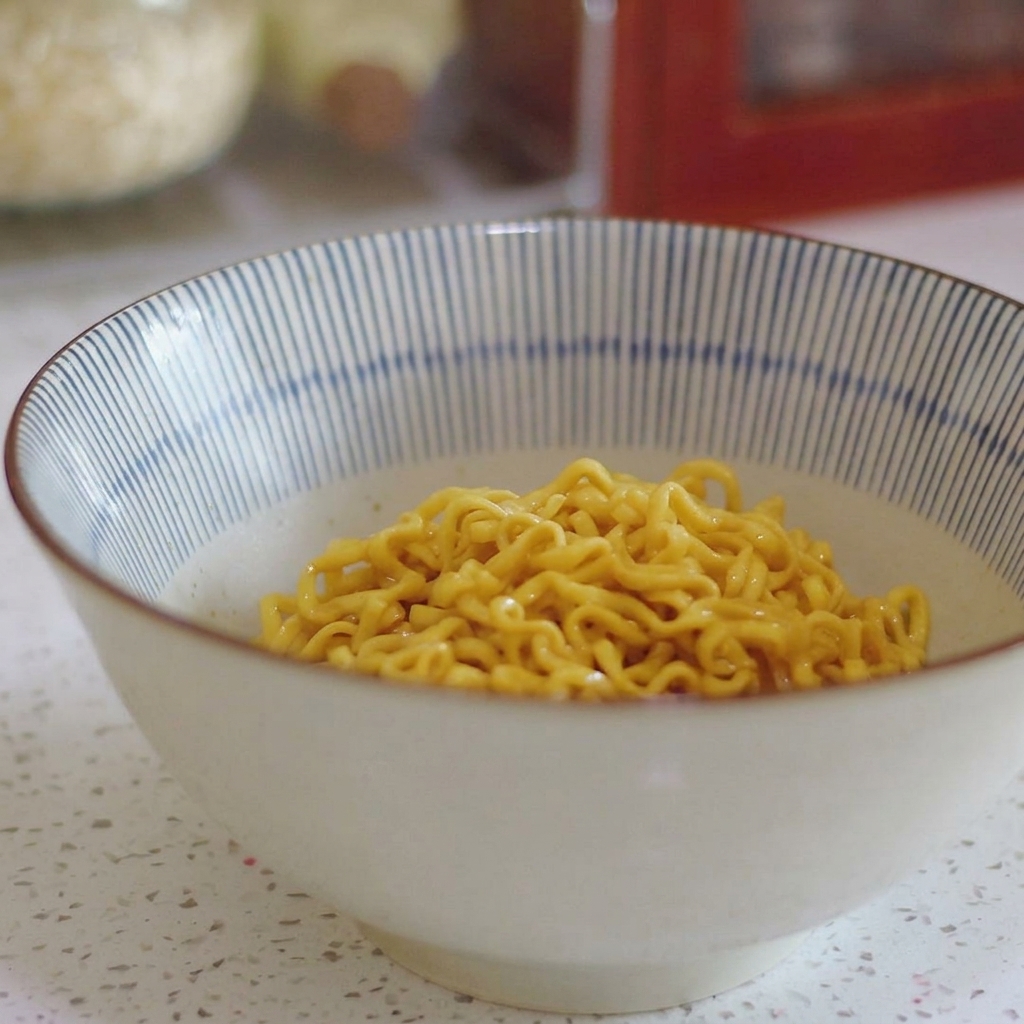 Yellow curly ramen noodles sitting in the bottom of a blue and white striped ceramic bowl.