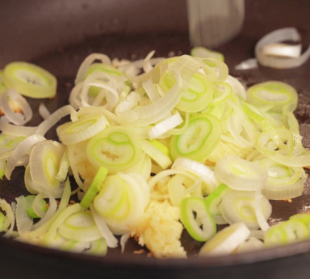 Raw ground pork, minced garlic, and a pile of sliced green onions sitting in a dark frying pan ready to be cooked.