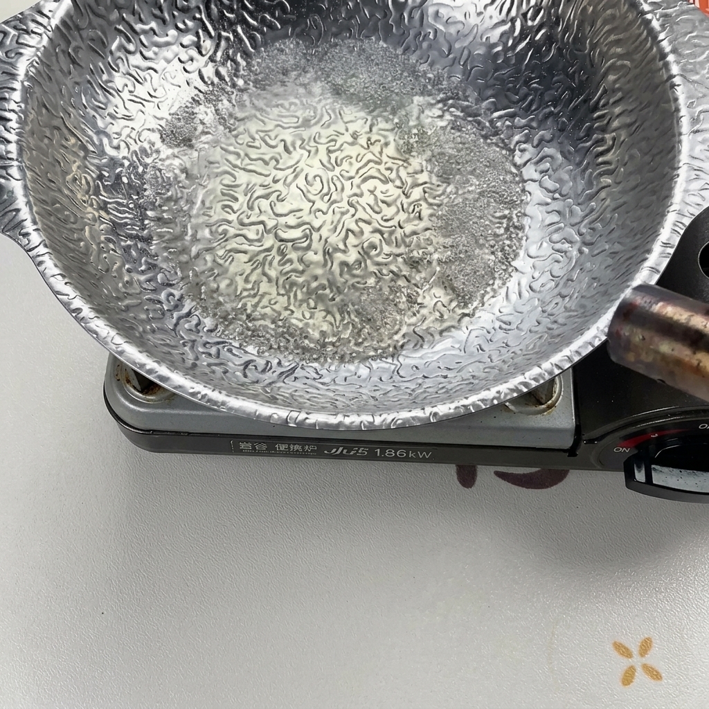 Liquid bubbling vigorously in a silver cooking pot as it is heated and ignited with a torch to remove the alcohol content.