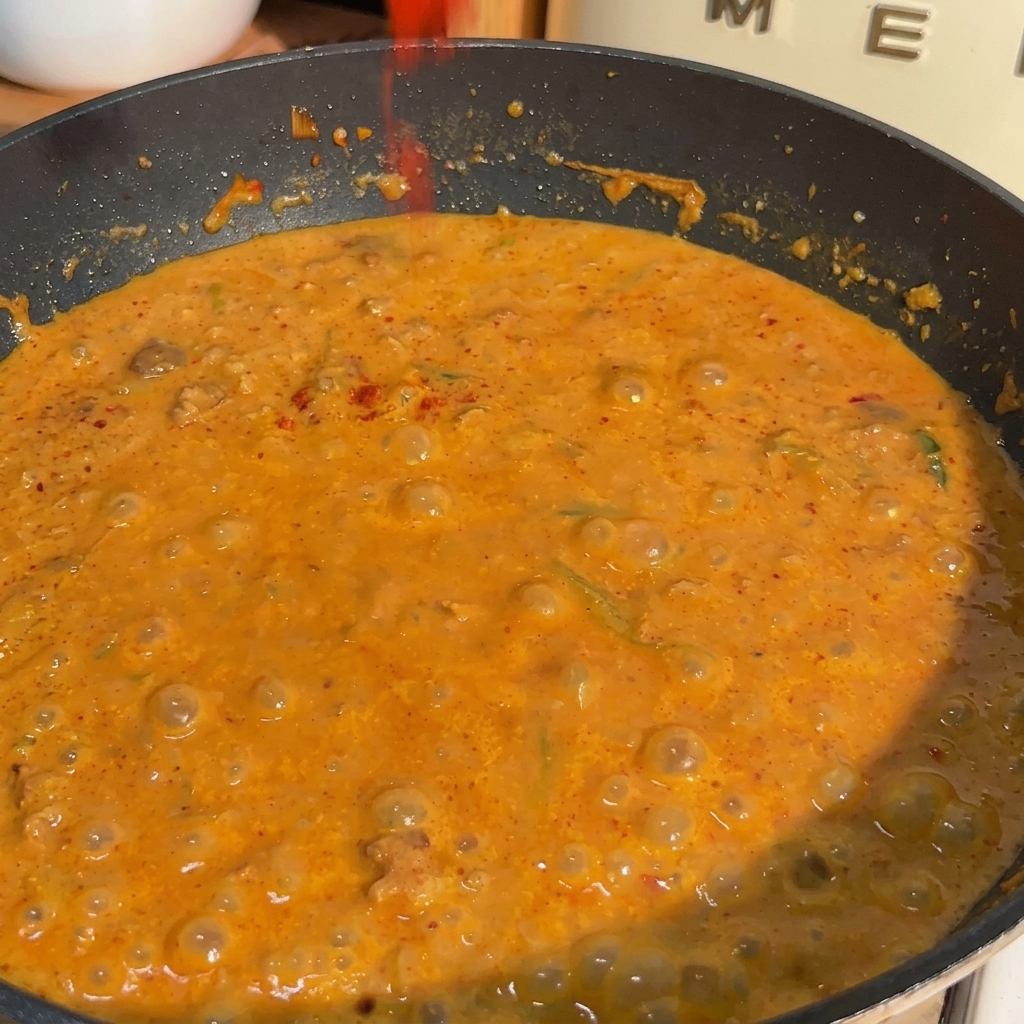 A pan filled with bubbling orange soy milk and miso sauce as red chili powder is sprinkled over the surface.