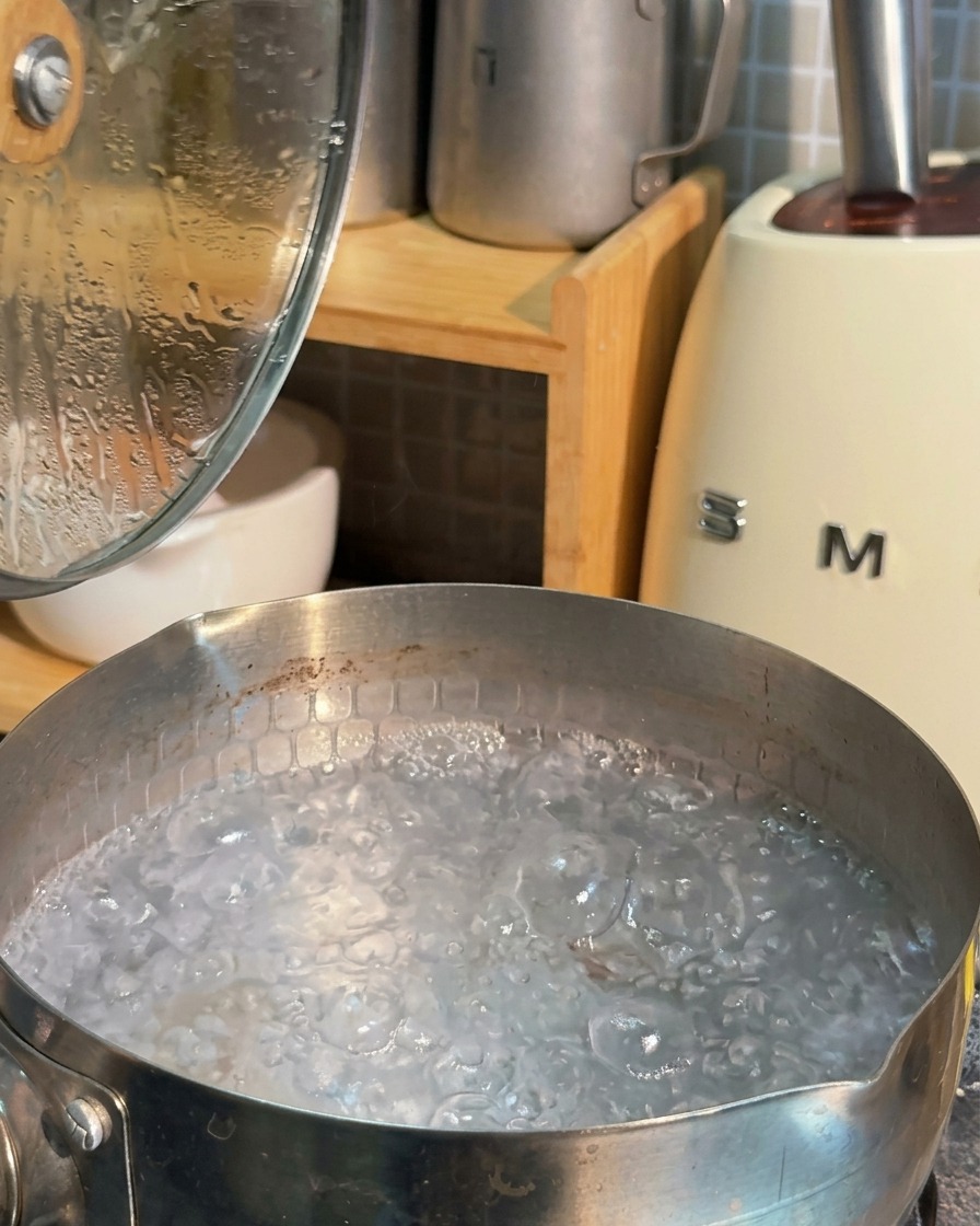 A stainless steel pot filled with rapidly boiling water and bubbling white foam.