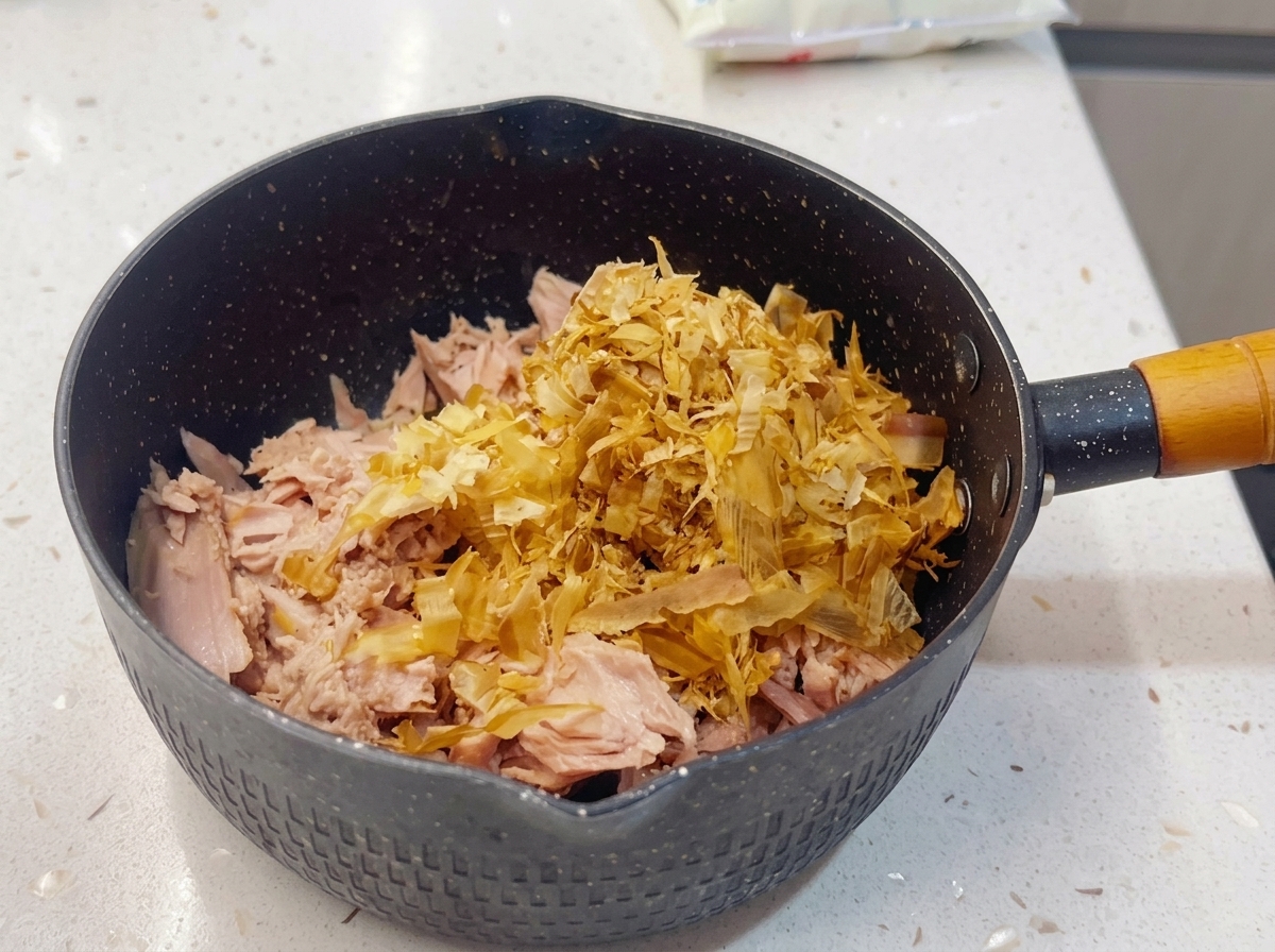 A small black pan filled with a layer of flaked canned tuna topped generously with a mound of dried bonito flakes.