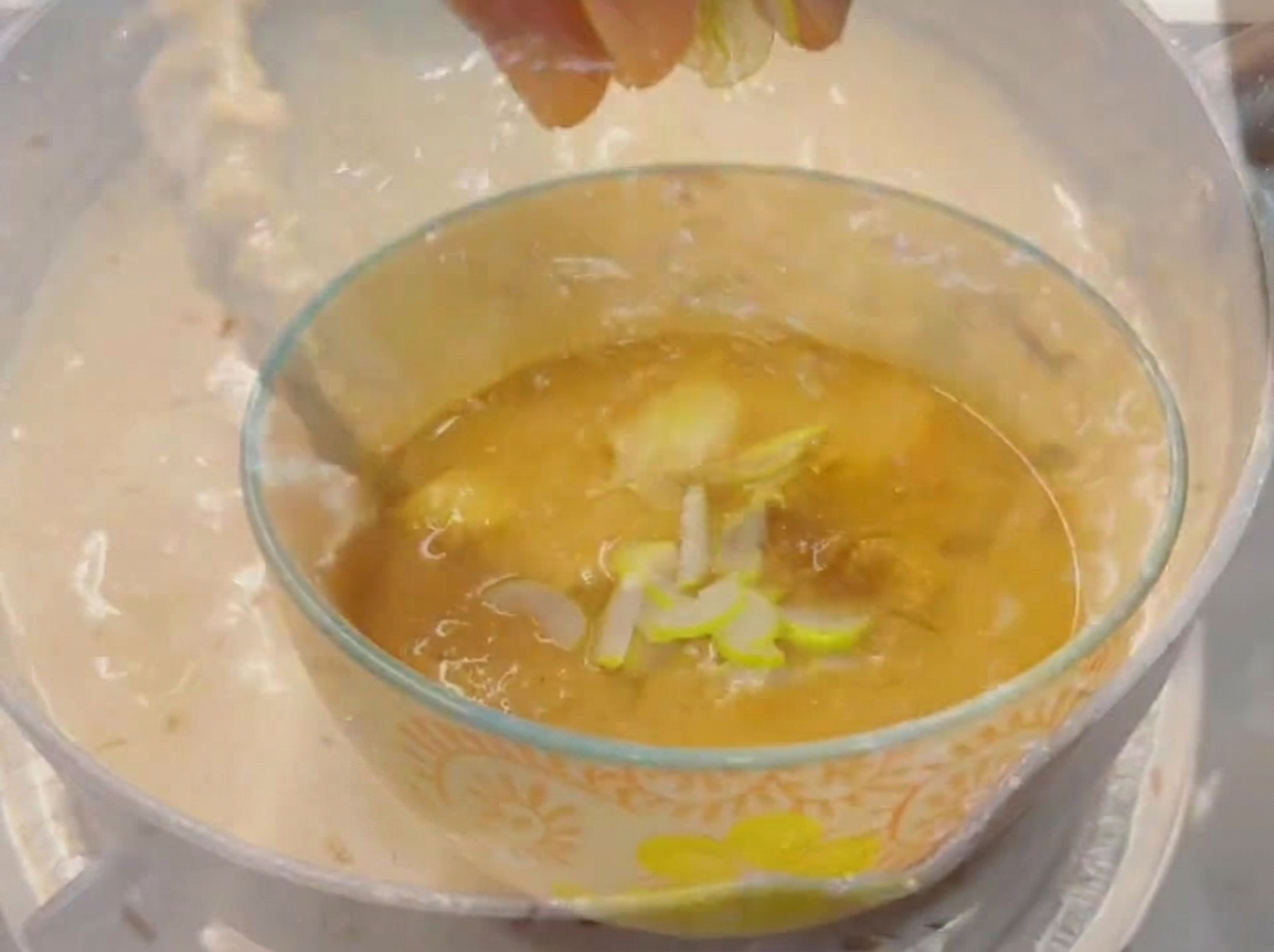 Fingertips dropping freshly chopped green scallions into a small glass bowl filled with a thick, savory dipping broth.