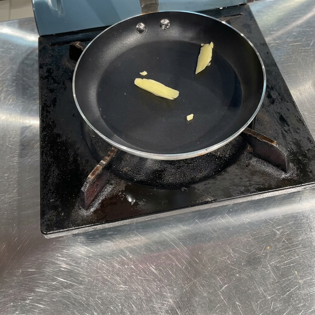 A small piece of yellow butter melting inside a black flat-bottomed pan on a stovetop.