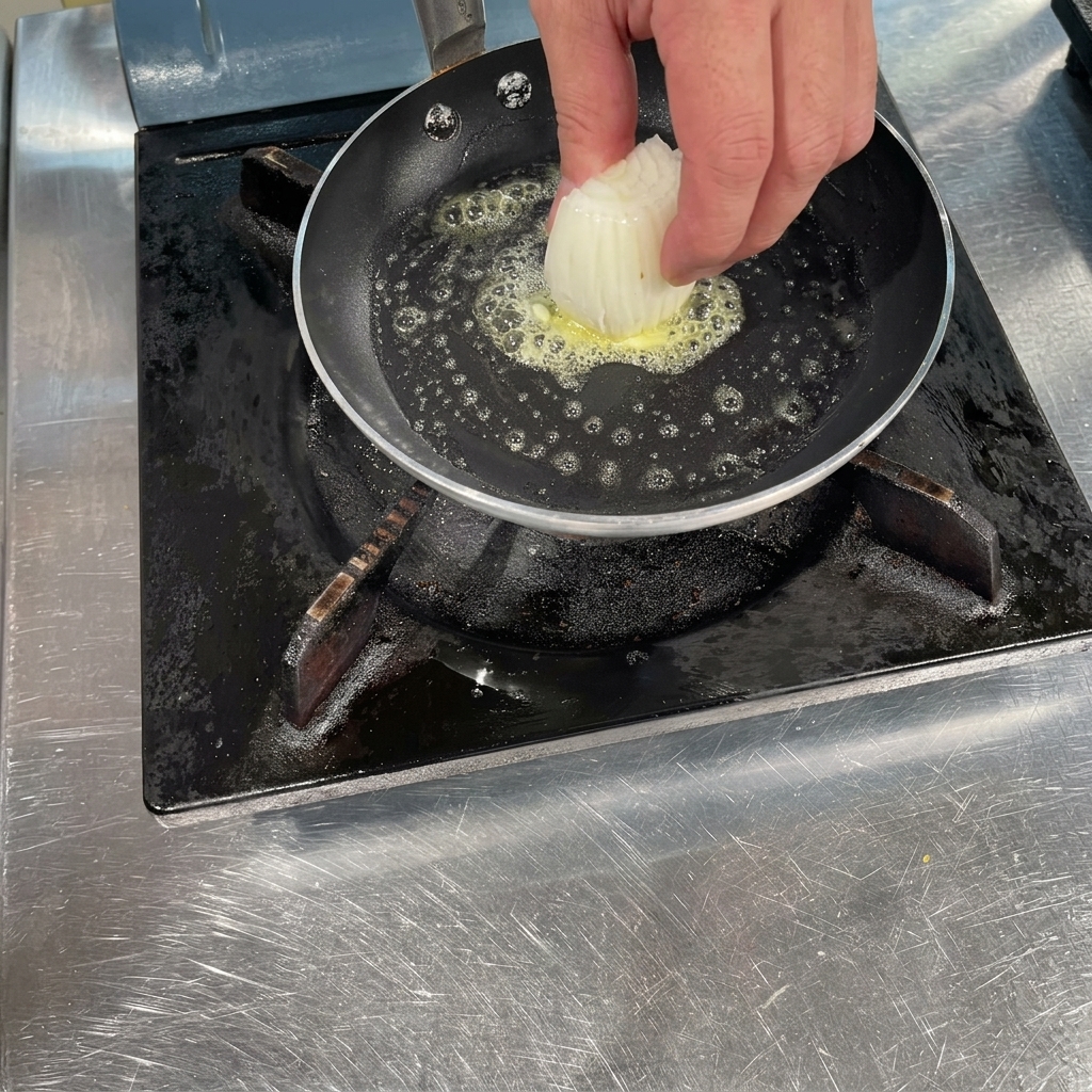 A hand placing a chunk of sliced white onions into a hot pan with bubbling melted butter.