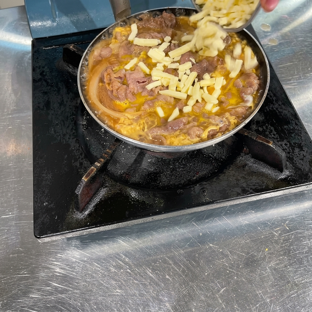 A hand sprinkling shredded white cheese over a pan filled with cooked beef, onions, and gently set egg.